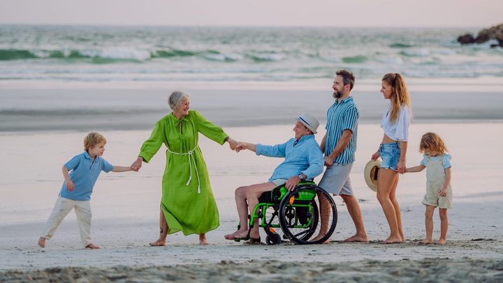 Familia en la playa con el abuelo en silla de ruedas