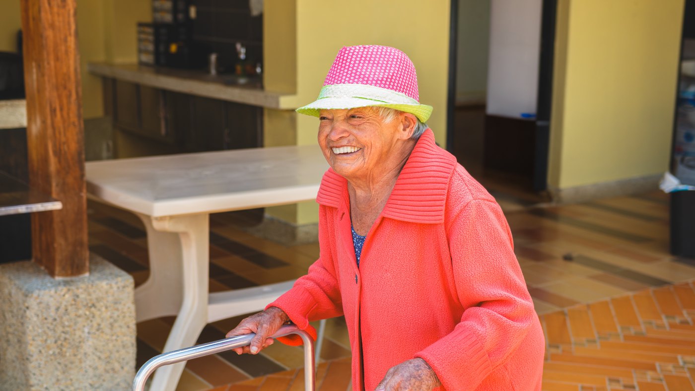 Adulta mayor sonriente con sombrero rosa paseando con su andadera en un día soleado