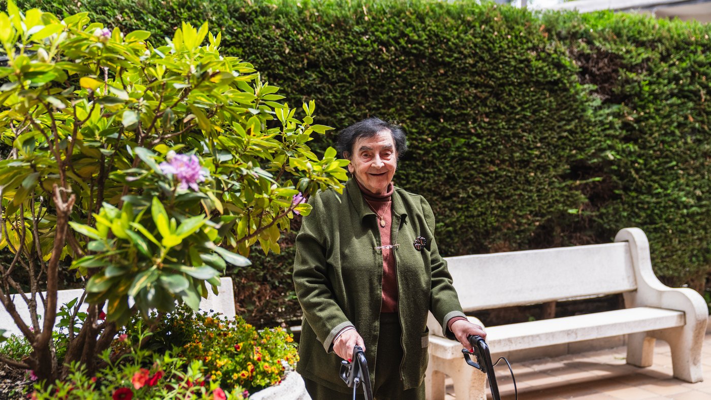 Adulta mayor sonriente de pie con su andadera con ruedas en un jardín