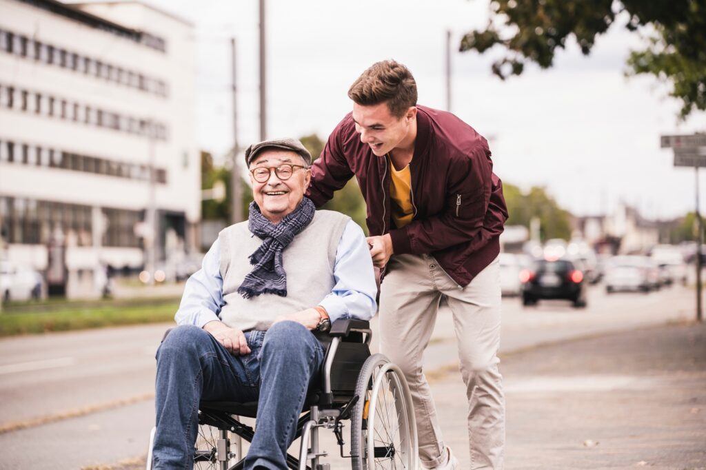 Young man pushing happy senior man in wheelchair